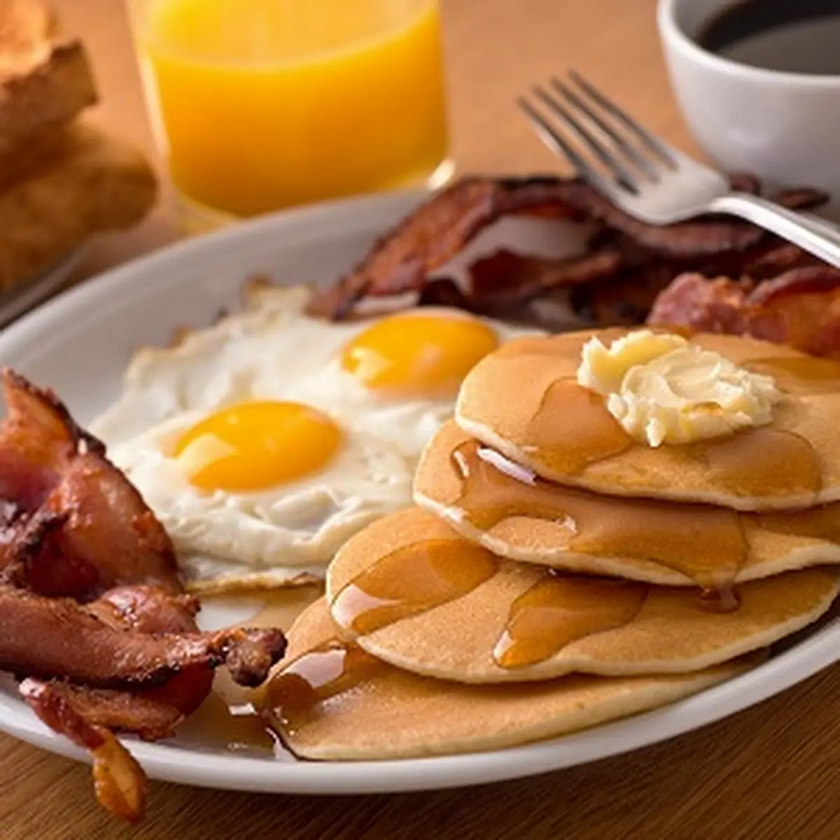Delicous Home Style Breakfast with Crispy Bacon Eggs Pancakes Toast Coffee and Orange Juice