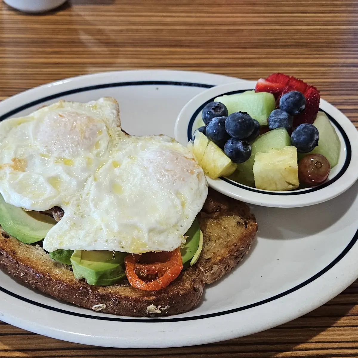 Avocado Toast with Fresh Fruit Top It Off with 2 Eggs & 2 Bacon Stripes
