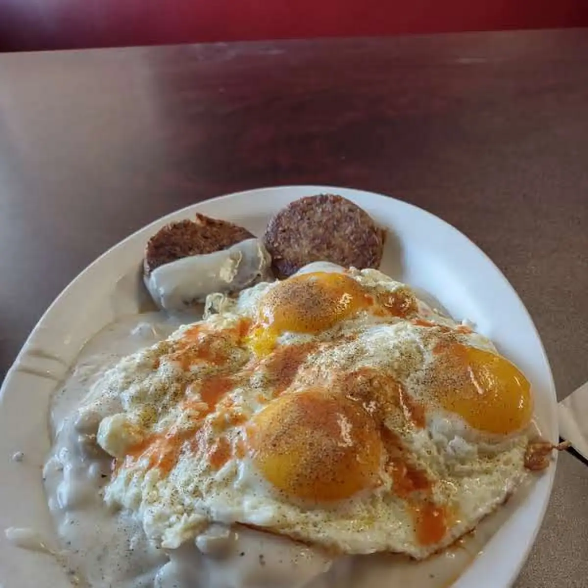 Biscuits and Gravy with 3 Sunny Side Up Eggs on Top with 2 Sausage Patties