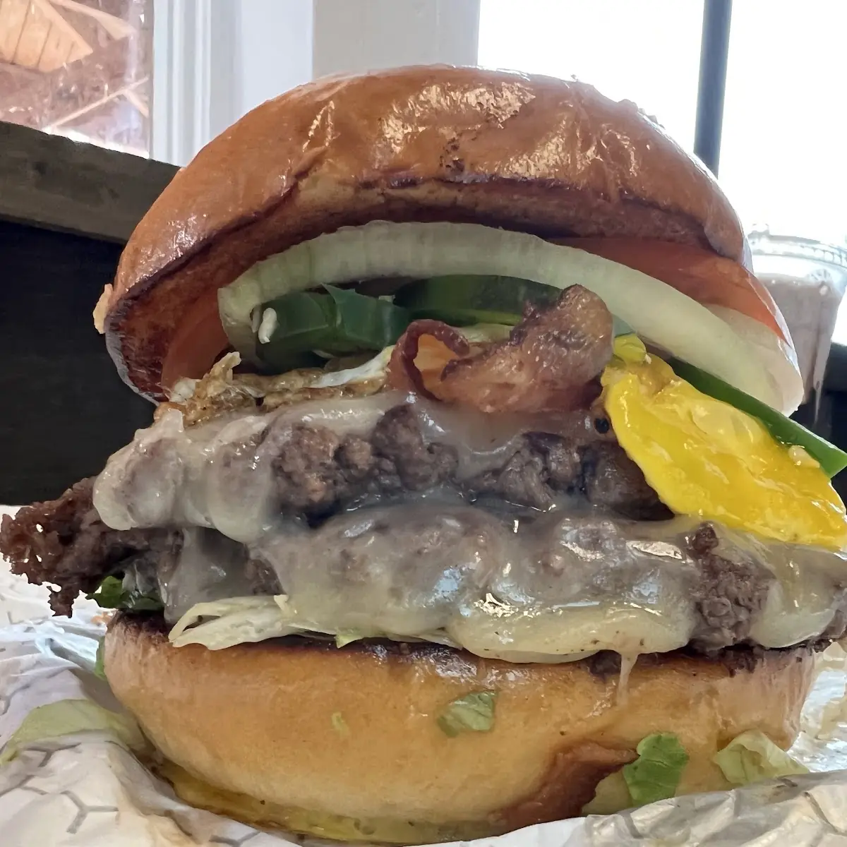 Bacon Cheeseburger with Lettuce Tomatoes Raw Onions Jalapeños and a Fried Egg