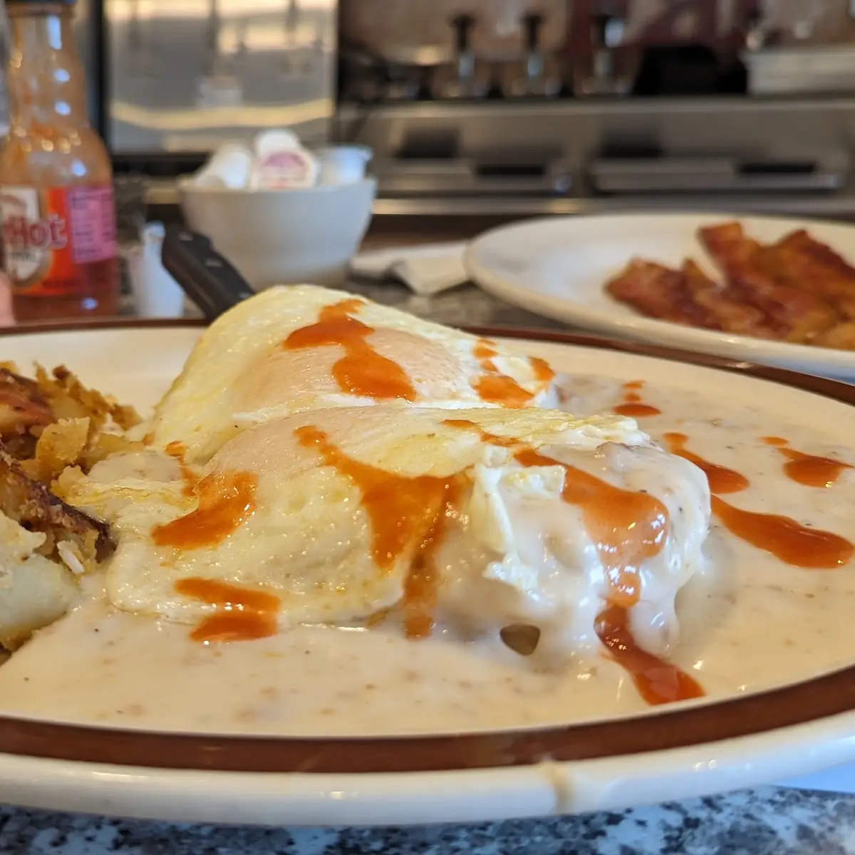 Sausage Gravy over Biscuits Top with Two over Easy Eggs Hash Brown Side of Bacon