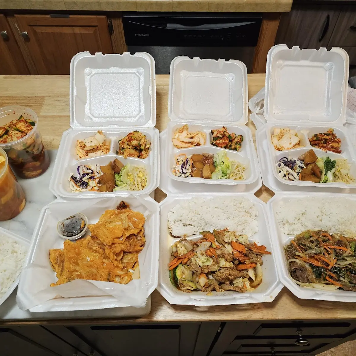 Pork Teriyaki Japchae Kimchi Pancakes Kimchi Soup Container of Cucumber Kimchi Rice and Vegetables