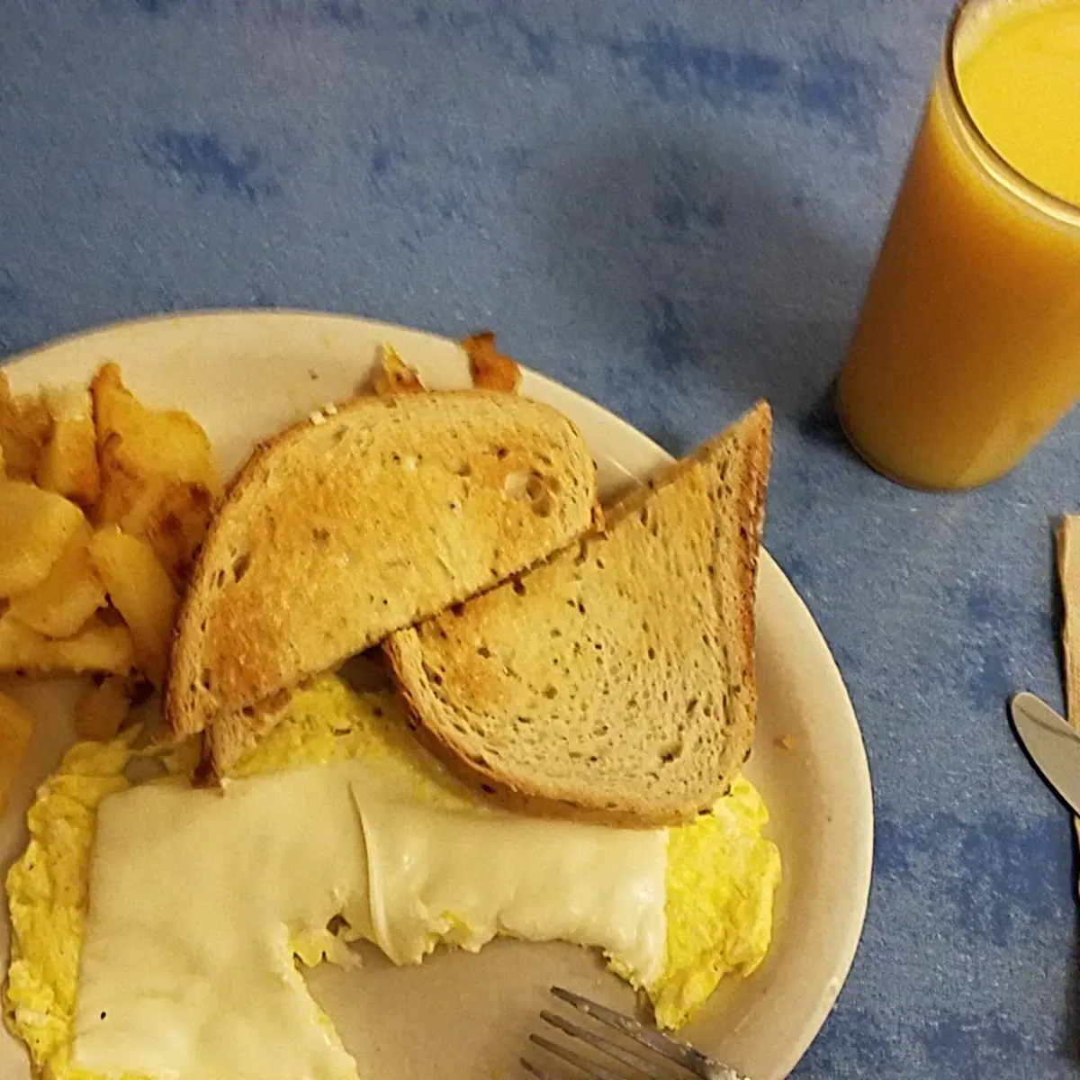 Scrambled Eggs Well Done with Cheese Melted in to Hash Brown Potatoes Toast and Small Orange Juice